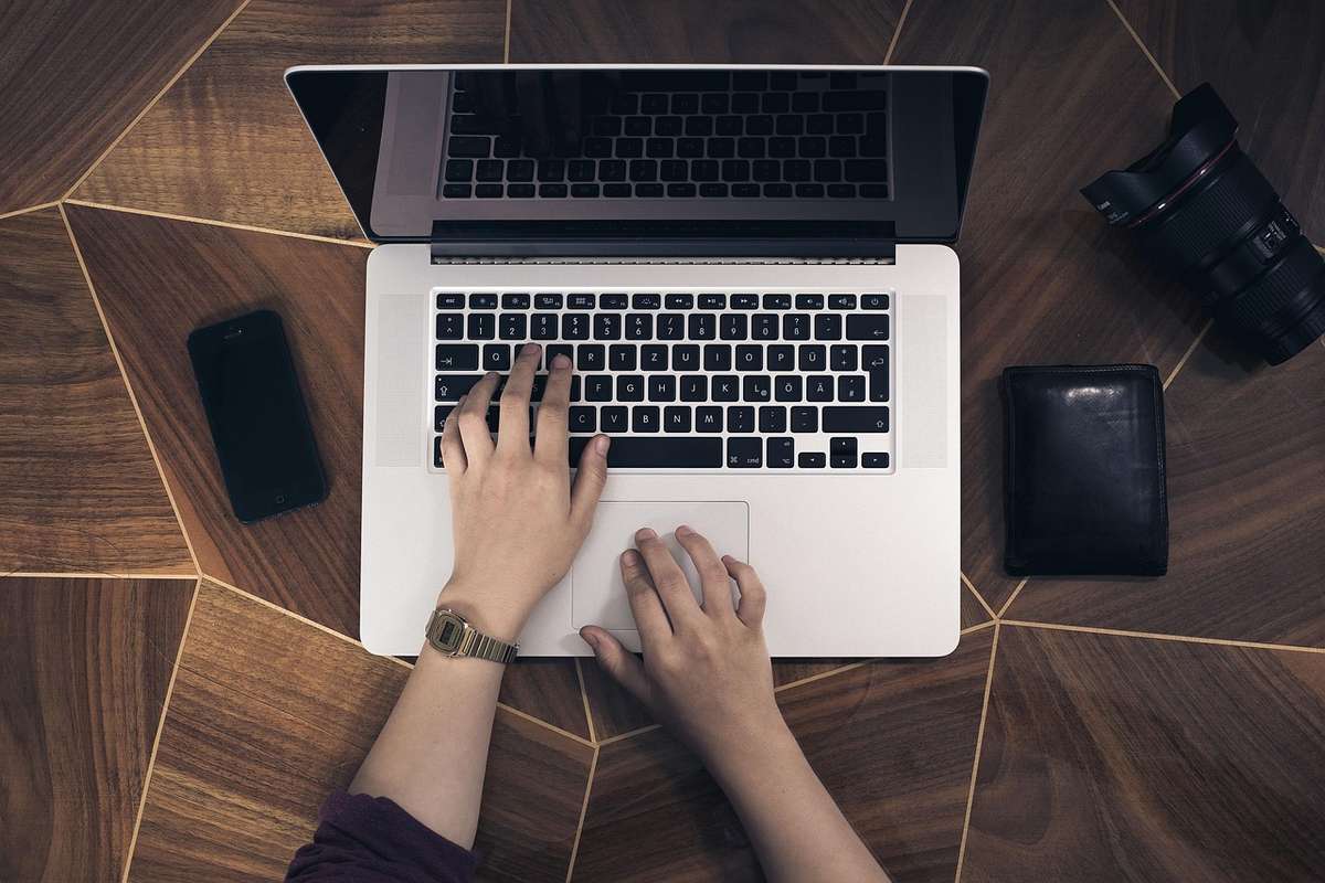 Mains d'une personne travaillant sur un laptop, vue de dessus, sur bureau en bois