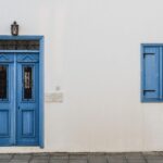 Porte et fenêtre bleues sur mur blanc avec lampe et pavés