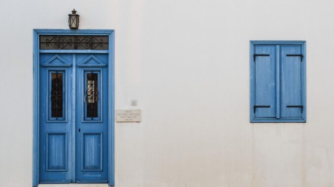 Porte et fenêtre bleues sur mur blanc avec lampe et pavés