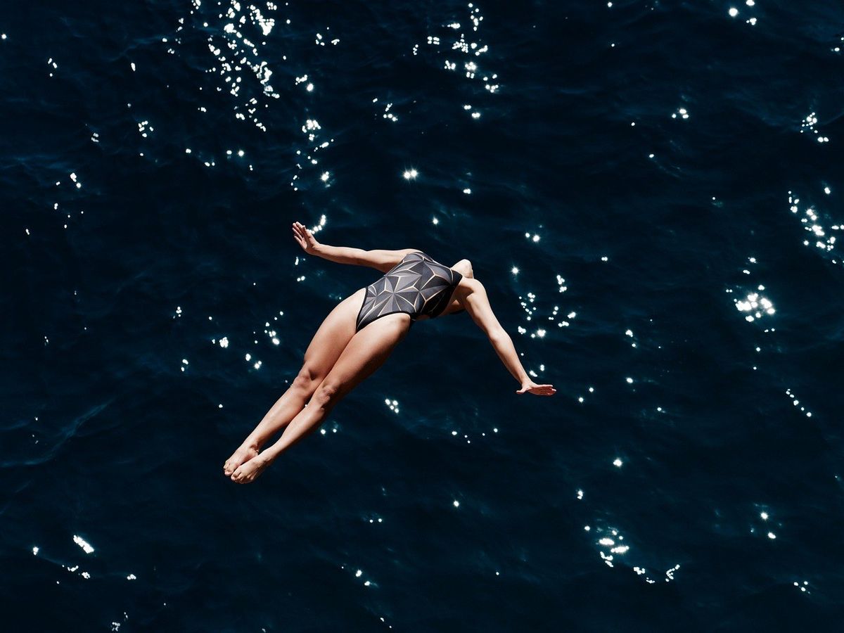 Femme en maille de bain nageant dans l'eau avec les bras tendus, soleil scintillant