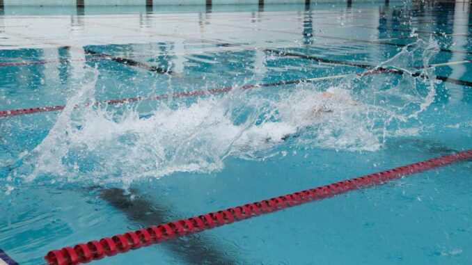 Nageur en pleine course dans une piscine, créant des éclaboussures d'eau